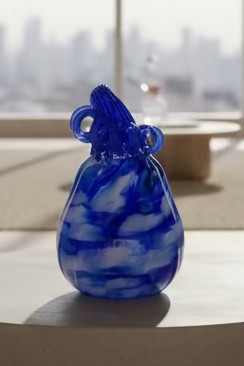 Blue glass bottle with a unique design on a wooden surface with other ceramic items in the background.